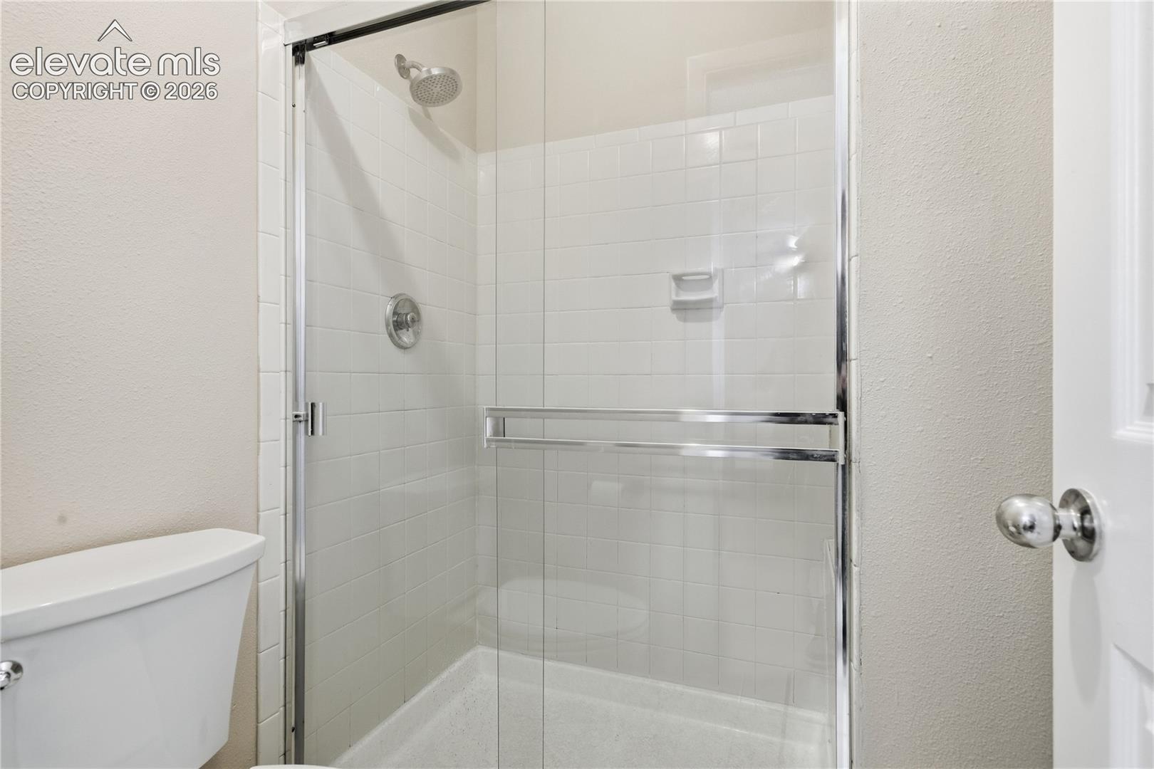 Enclosed shower with clear glass surround, white tiled walls, and a chrome showerhead