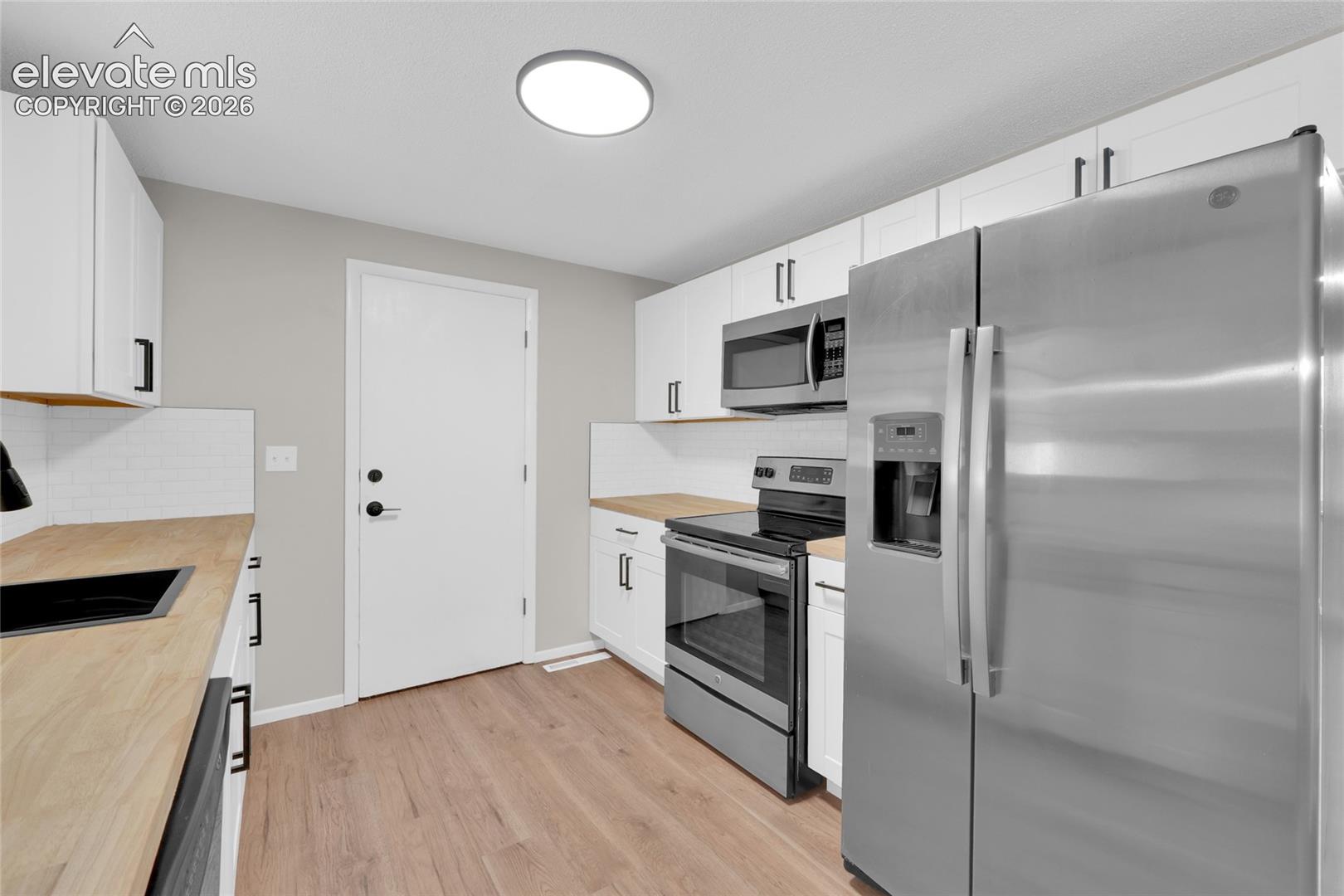 Kitchen featuring wood-finish flooring, white cabinetry with black hardware, wood-finish countertops, subway tile backsplash, and stainless steel appliances