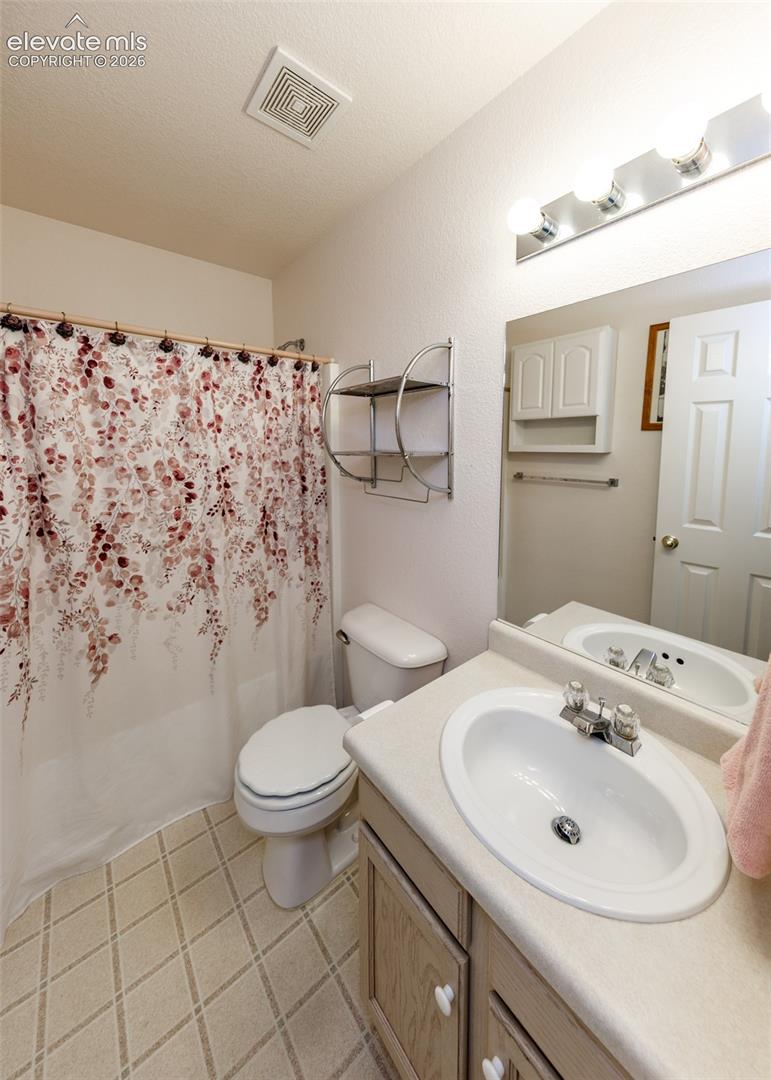 Bathroom featuring a single-sink vanity with a solid-surface countertop, wall-mounted three-light fixture, large rectangular mirror, and built-in wall cabinet