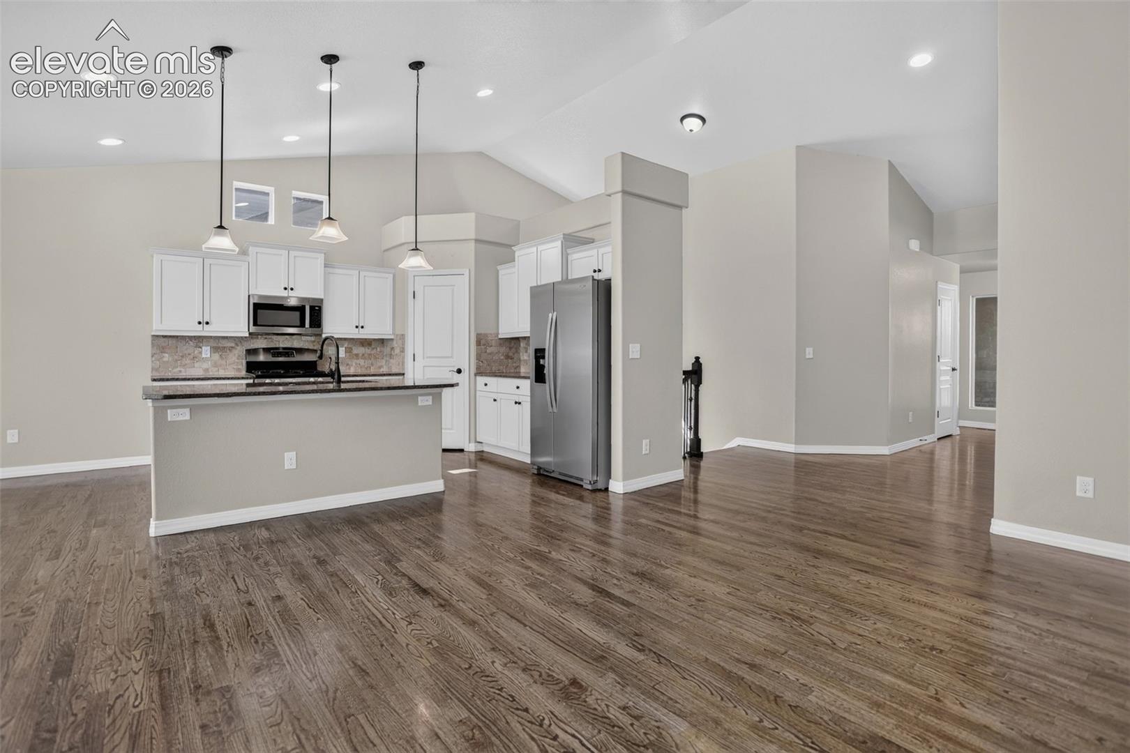 Open-concept living area with wood-finish flooring, vaulted ceilings, and recessed lighting