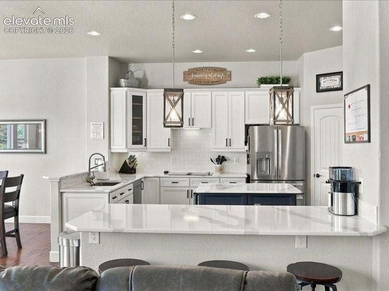 White shaker cabinetry, stainless steel appliances, white subway tile backsplash, white countertop surfaces, and a central island with a contrasting base