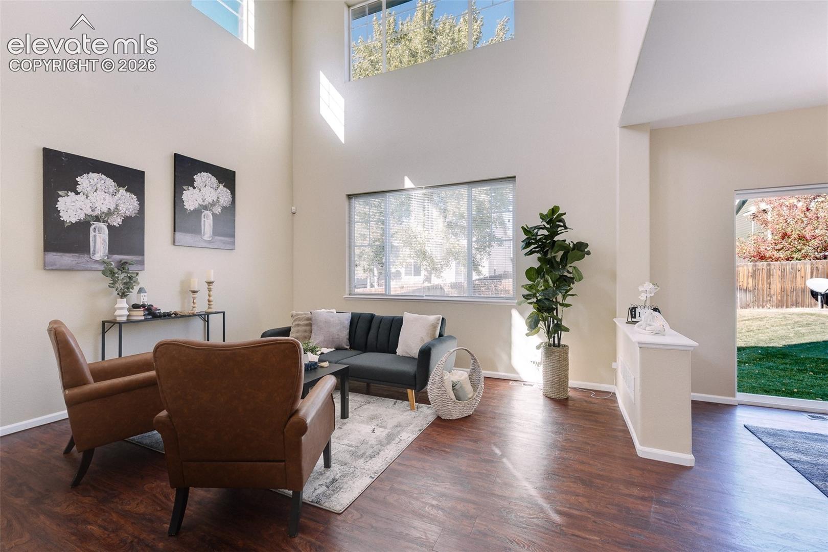 Living area featuring soaring vaulted ceilings, wood-finish flooring, expansive windows, and a sliding glass door providing external access