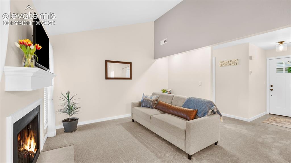 Living area featuring a fireplace with a white mantel, neutral wall paint, and vaulted ceilings