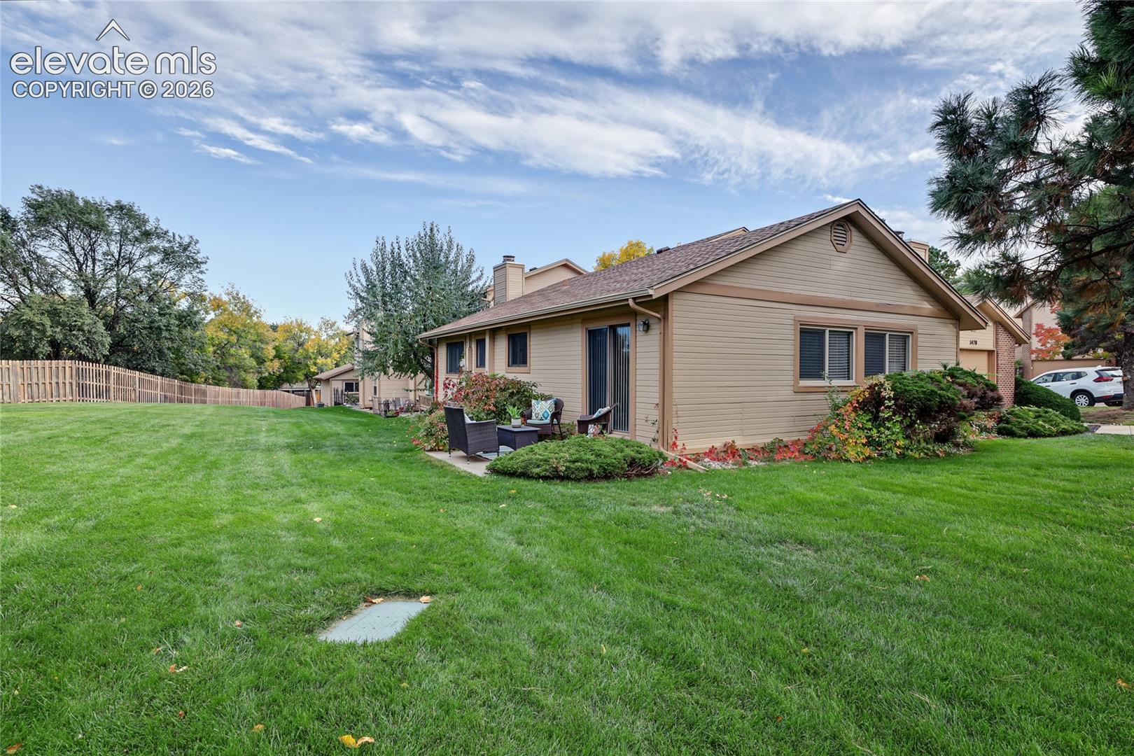 Expansive grass yard with wood fencing, mature trees, a side patio, and a sliding glass door