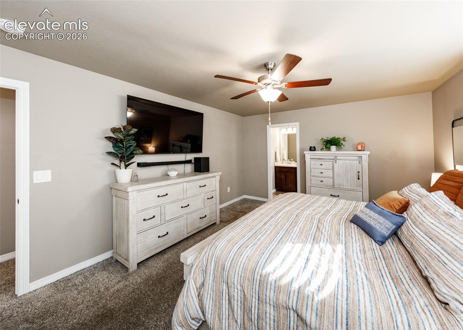 Neutral-toned bedroom featuring plush wall-to-wall carpeting, a central ceiling fan with integrated lighting, and uniform light-colored wall paint
