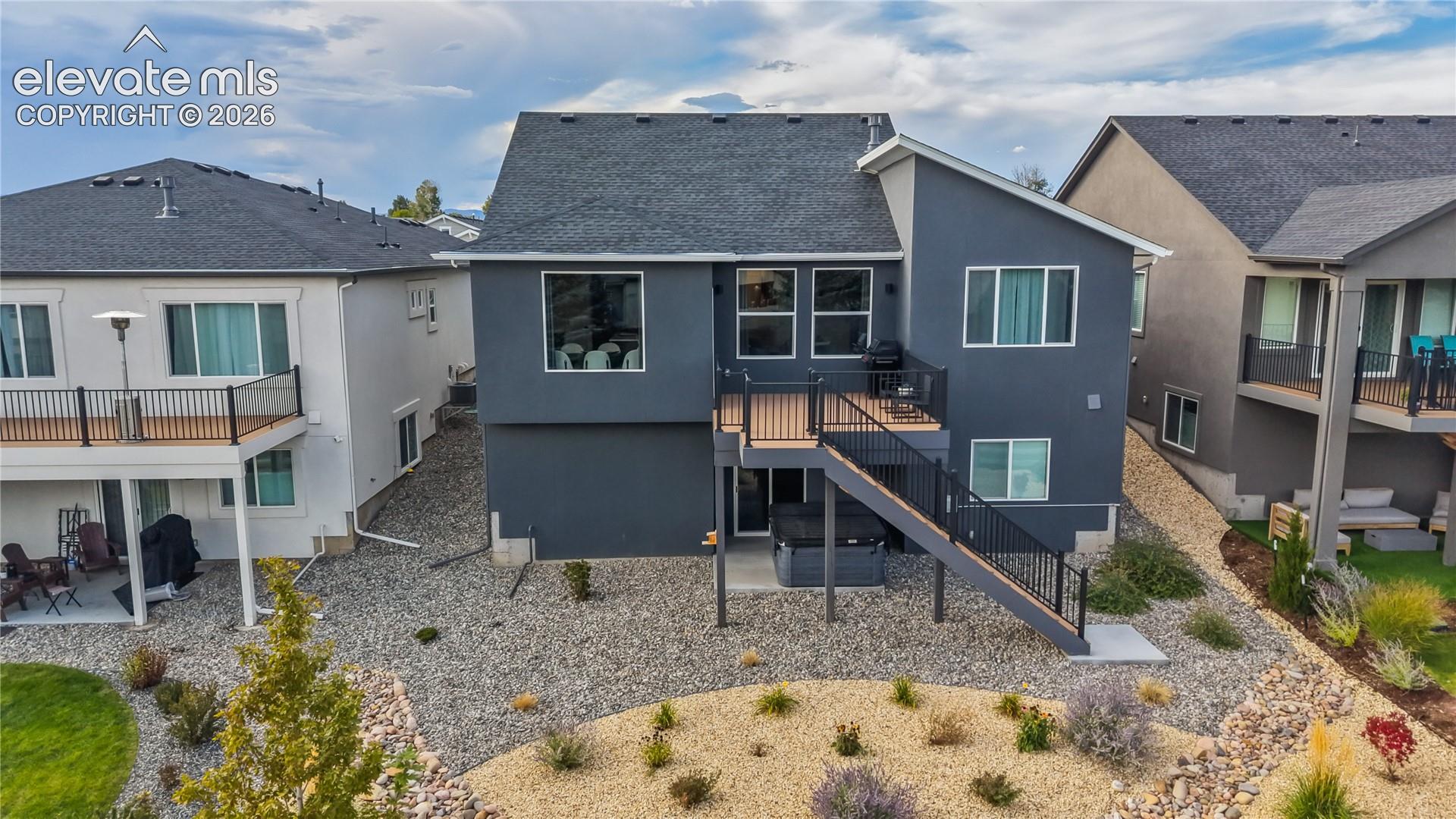 Two-story exterior featuring dark-toned siding, asphalt shingle roofing, an elevated composite deck with metal railing, and a stone-landscaped backyard