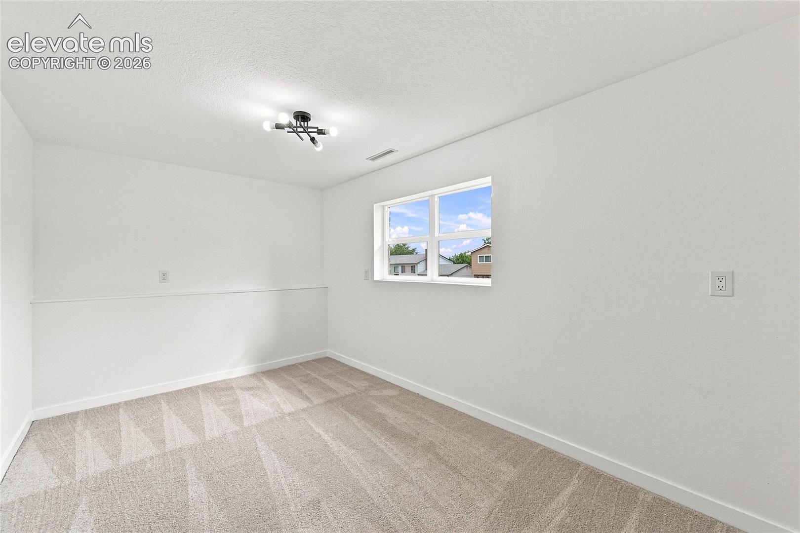 Neutral tone wall paint, contemporary ceiling light fixture, window with exterior scenery, wall-to-wall carpeting, and white trim