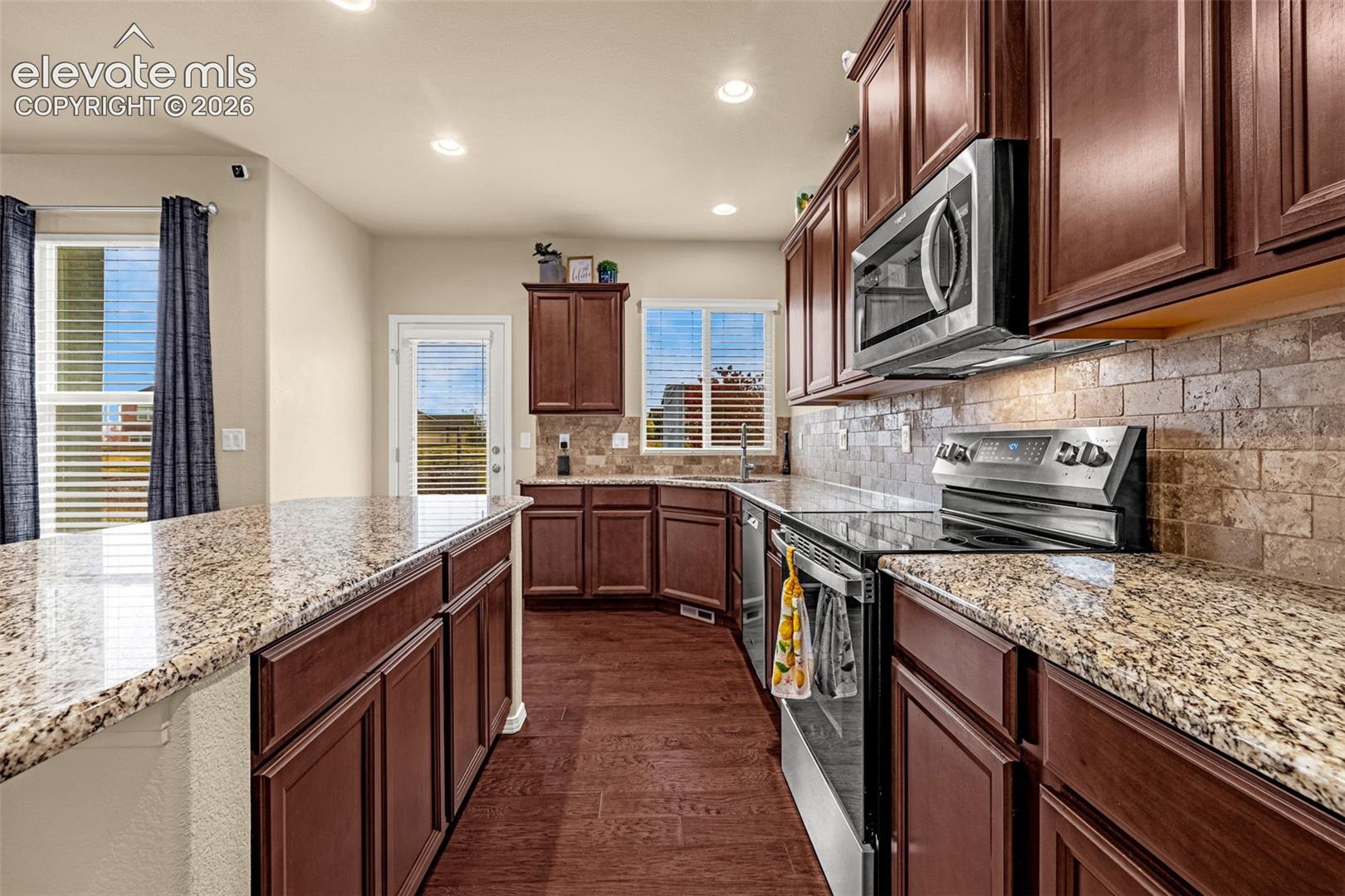 Kitchen featuring stained wood cabinetry, stone-surface countertops, textured tile backsplash, stainless steel appliances, and recessed lighting