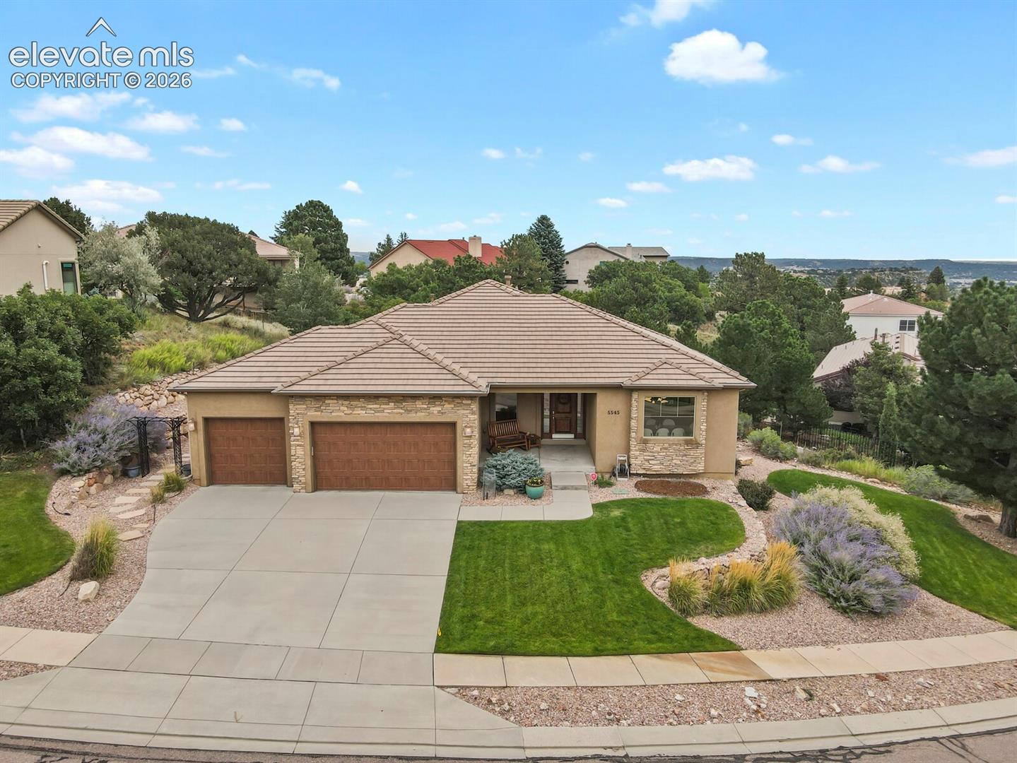Tan single-story home with stone accents, a two-car garage, and landscaped front yard, viewed from above.