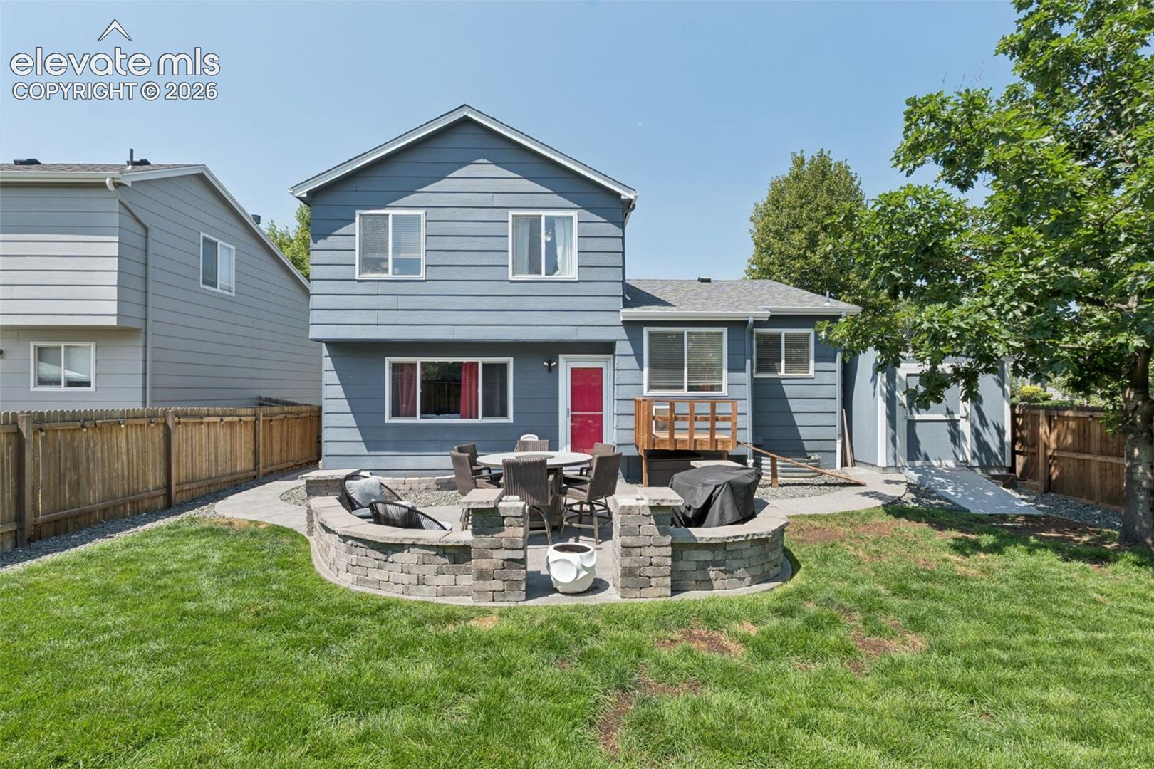 Expansive backyard with a manicured lawn, a stone-built patio, and a dedicated fire pit area