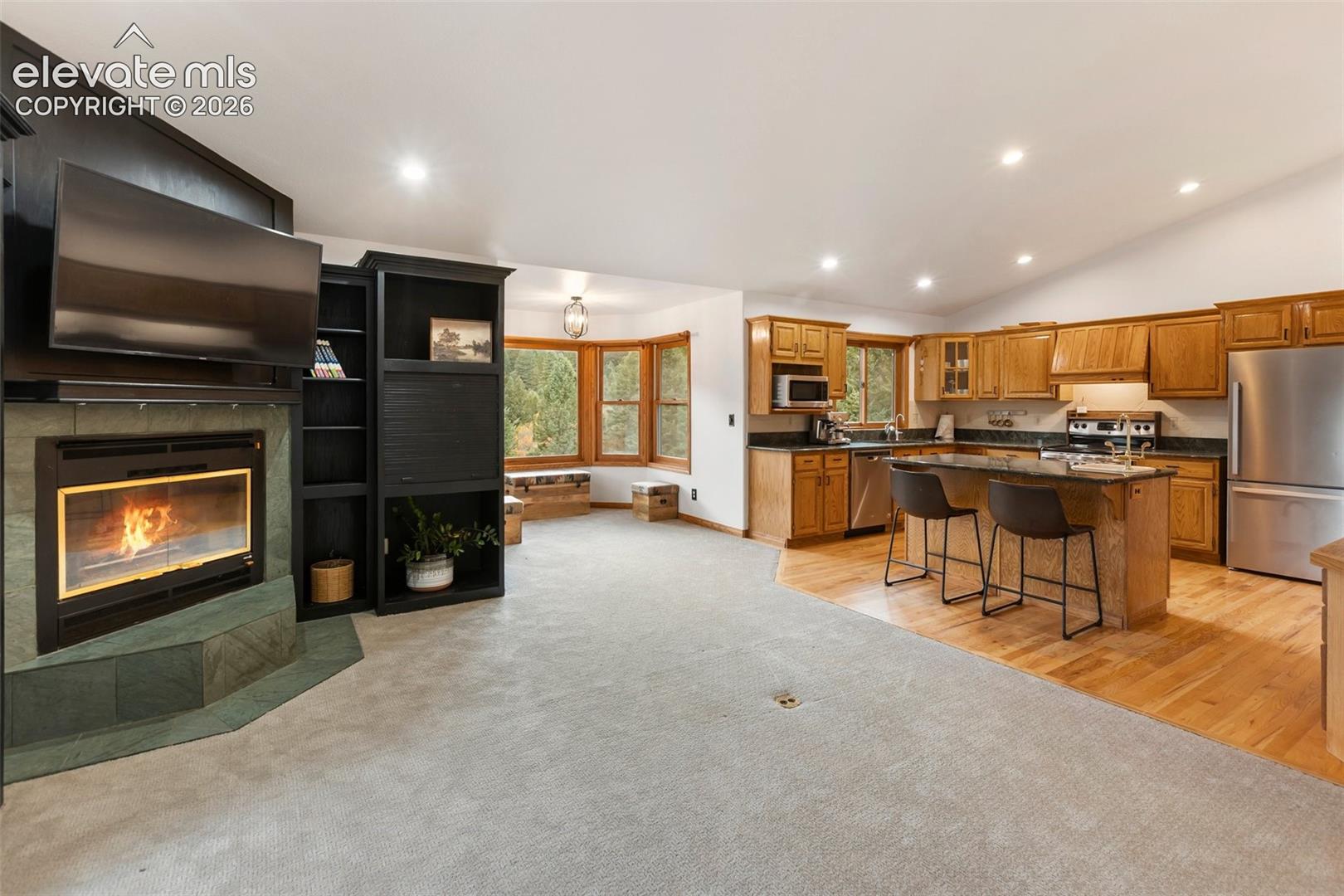 Fireplace with a stone surround and built-in black cabinetry, kitchen featuring wood cabinetry and an island with a stone countertop, and bay windows
