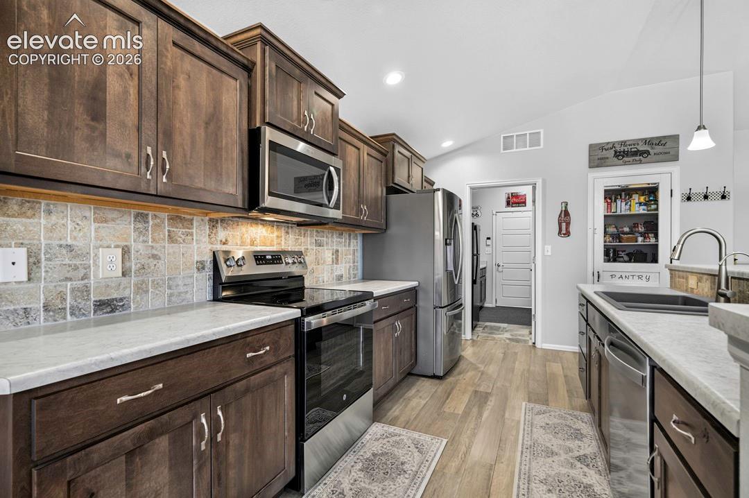 Kitchen featuring wood-finish cabinetry, light-toned countertops, stainless steel appliances, a tiled backsplash, and wood-finish flooring