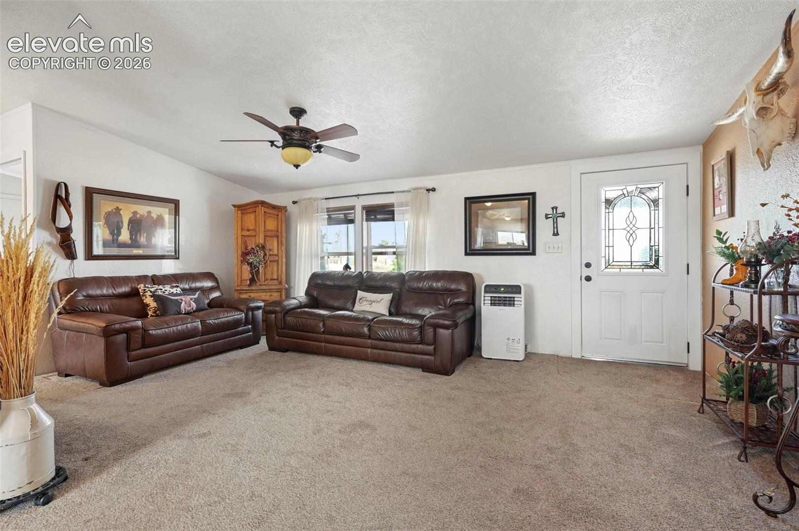 Living area featuring neutral carpeting, a ceiling fan with light fixture, and an exterior door with decorative glass paneling