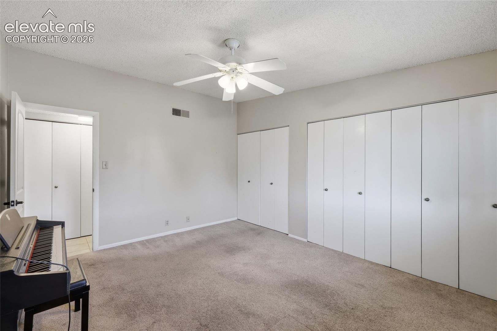 Spacious interior featuring neutral wall tones, wall-to-wall carpeting, multiple sets of white bi-fold closet doors, and a central ceiling fan with integrated lighting