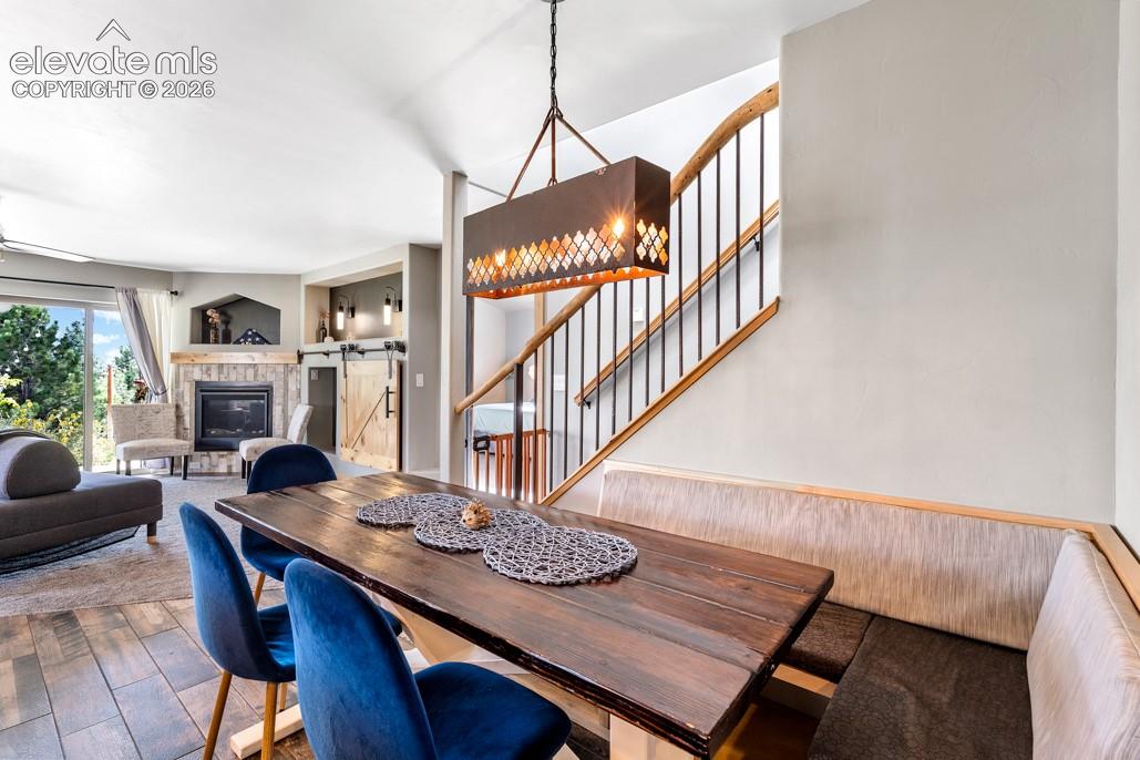 Built-in dining bench, wood-finish flooring, stone-surround fireplace, barn door, and a staircase with wood railing and iron balusters