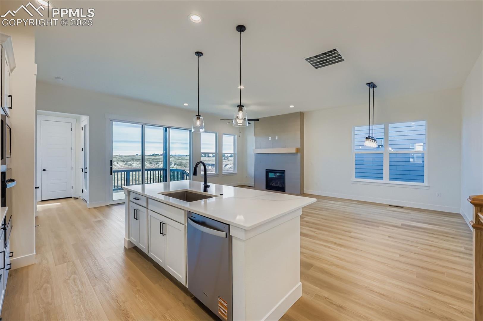 Kitchen featuring white cabinets, a fireplace, open floor plan, decorative light fixtures, and stainless steel dishwasher
