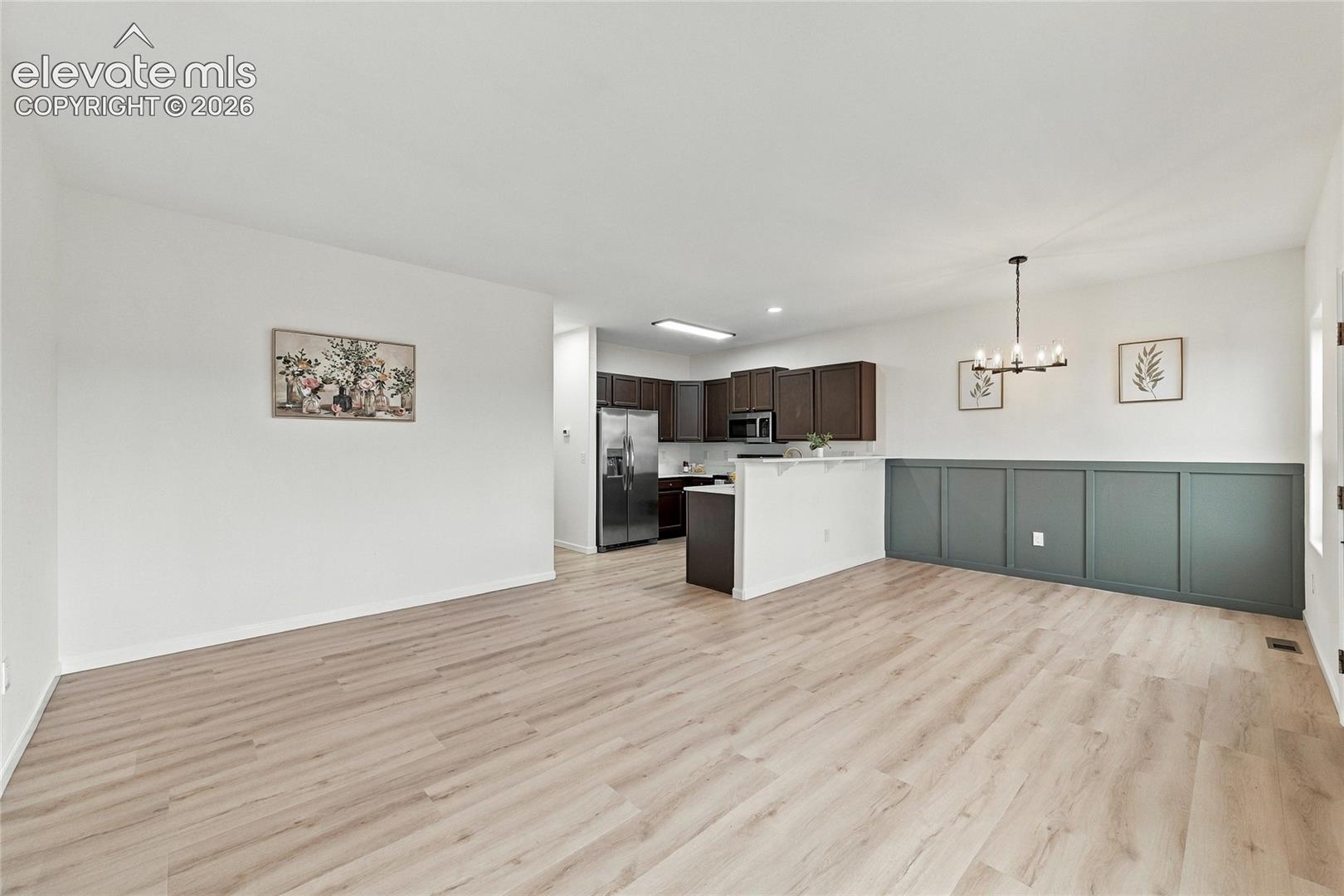 Open-concept interior featuring wood-finish flooring, paneled wainscoting, a multi-arm chandelier, and cabinetry in a dark finish