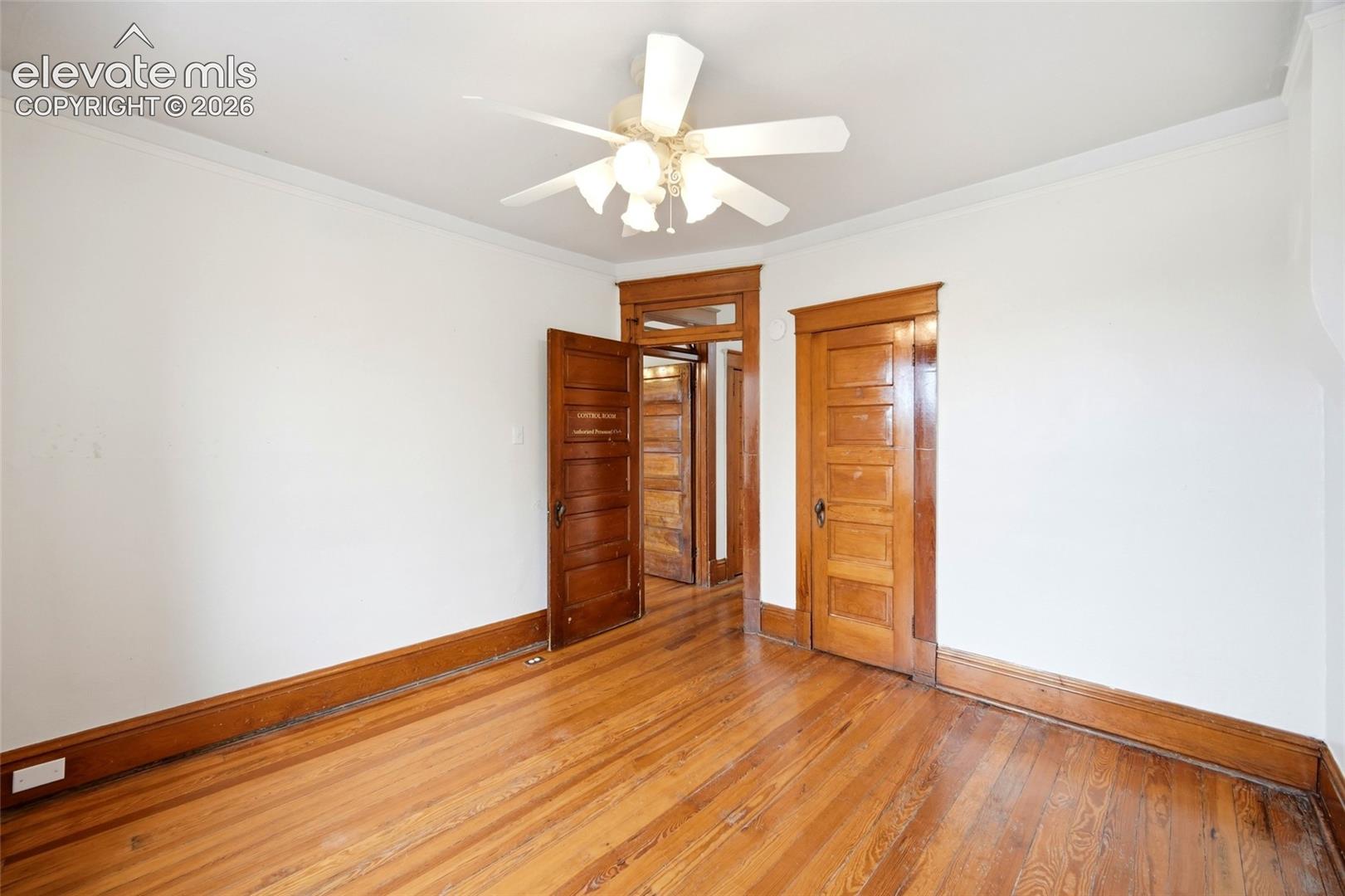 Room featuring wood-finish flooring, natural wood-tone interior doors with matching trim, and a multi-blade ceiling fan with integrated lighting