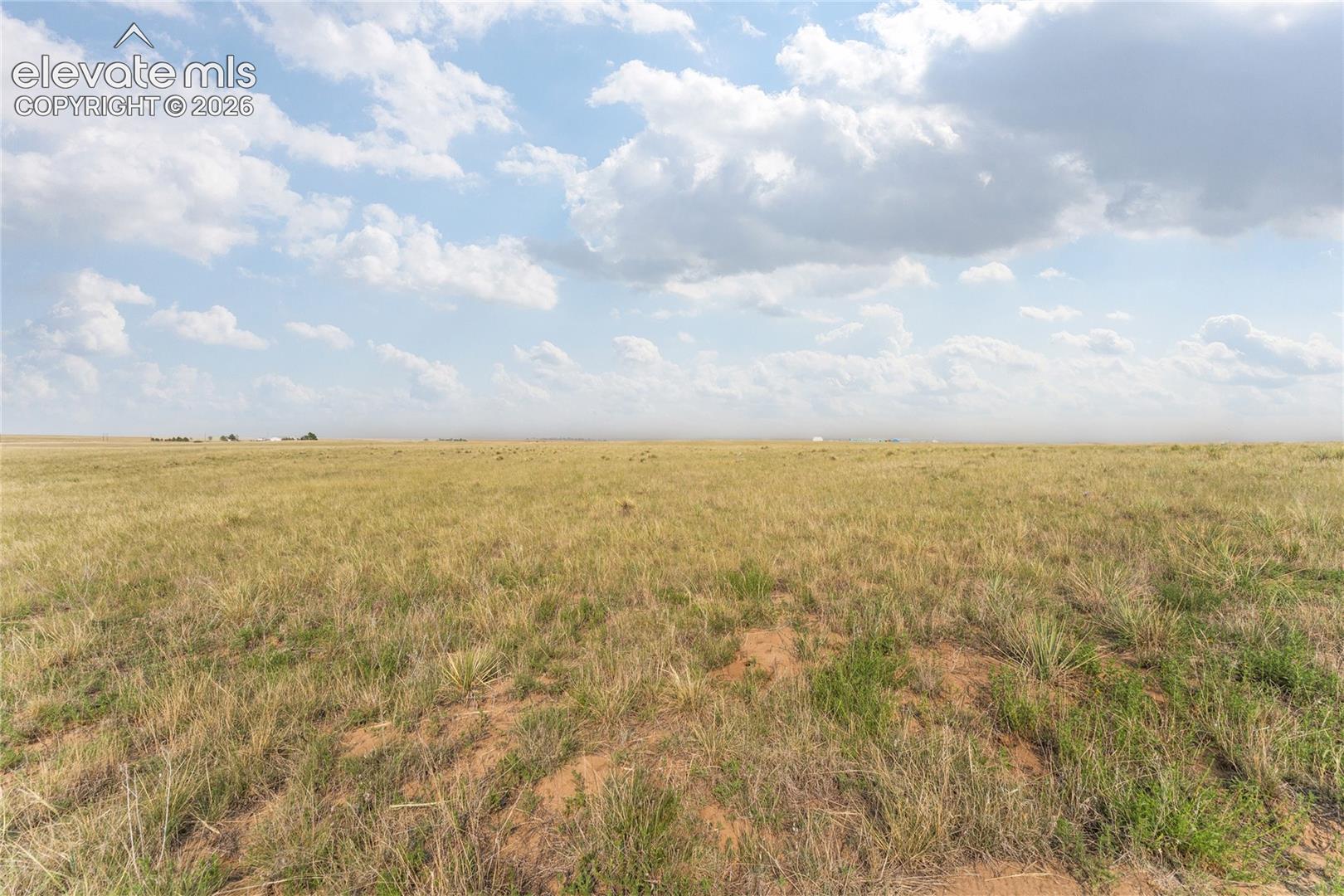 Expansive open land featuring natural grasses and distant structures under a broad sky