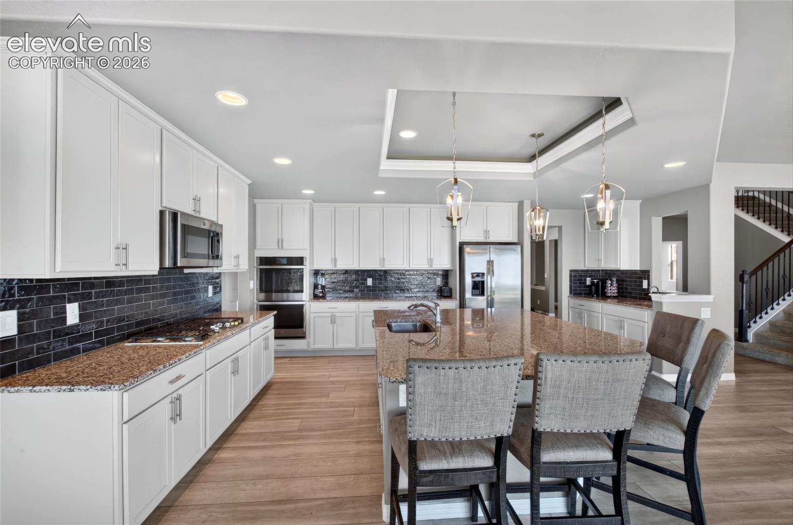 Spacious kitchen featuring white cabinetry, dark brick-patterned backsplash, light wood-finish flooring, and a large central island with pendant lighting