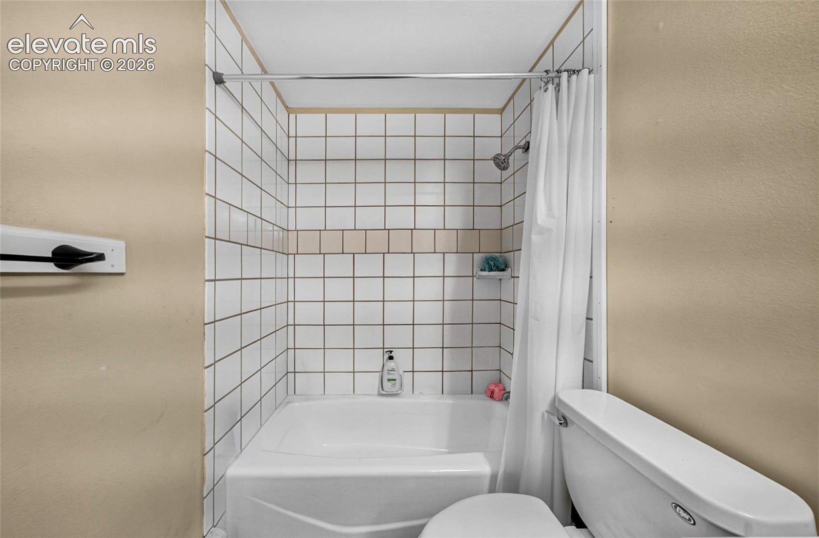 Recessed tub with a white ceramic tile surround featuring a contrasting decorative tile band, chrome shower fixture, and wall-mounted soap niche