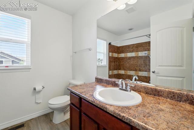 Full bathroom with vanity, toilet, a shower, wood finished floors, and baseboards