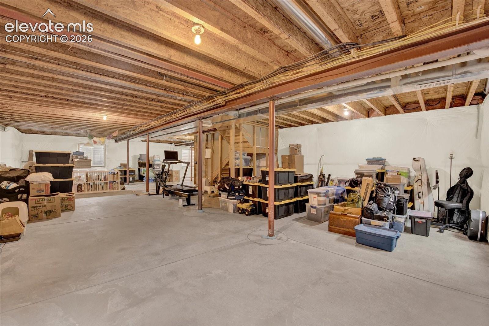 Unfinished lower level featuring concrete flooring, exposed wood joist ceiling, steel support columns, and interior wooden staircase