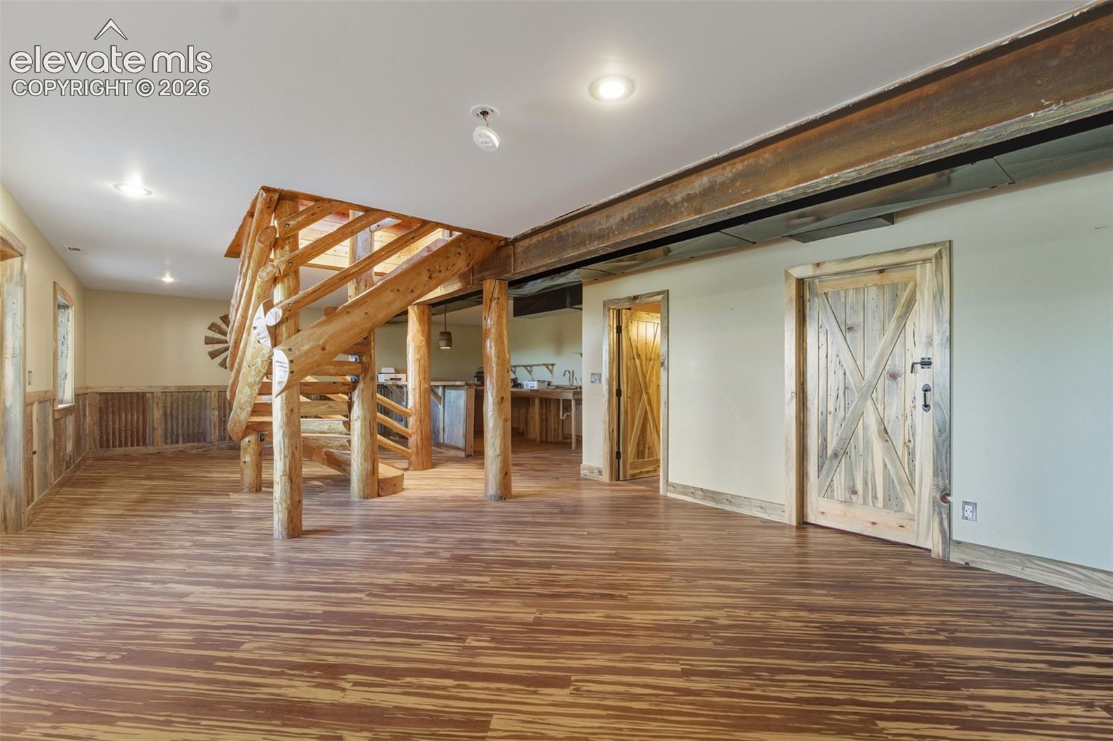 Wood-finish flooring throughout, featuring a custom wood staircase, exposed ceiling beam, and wooden barn-style doors