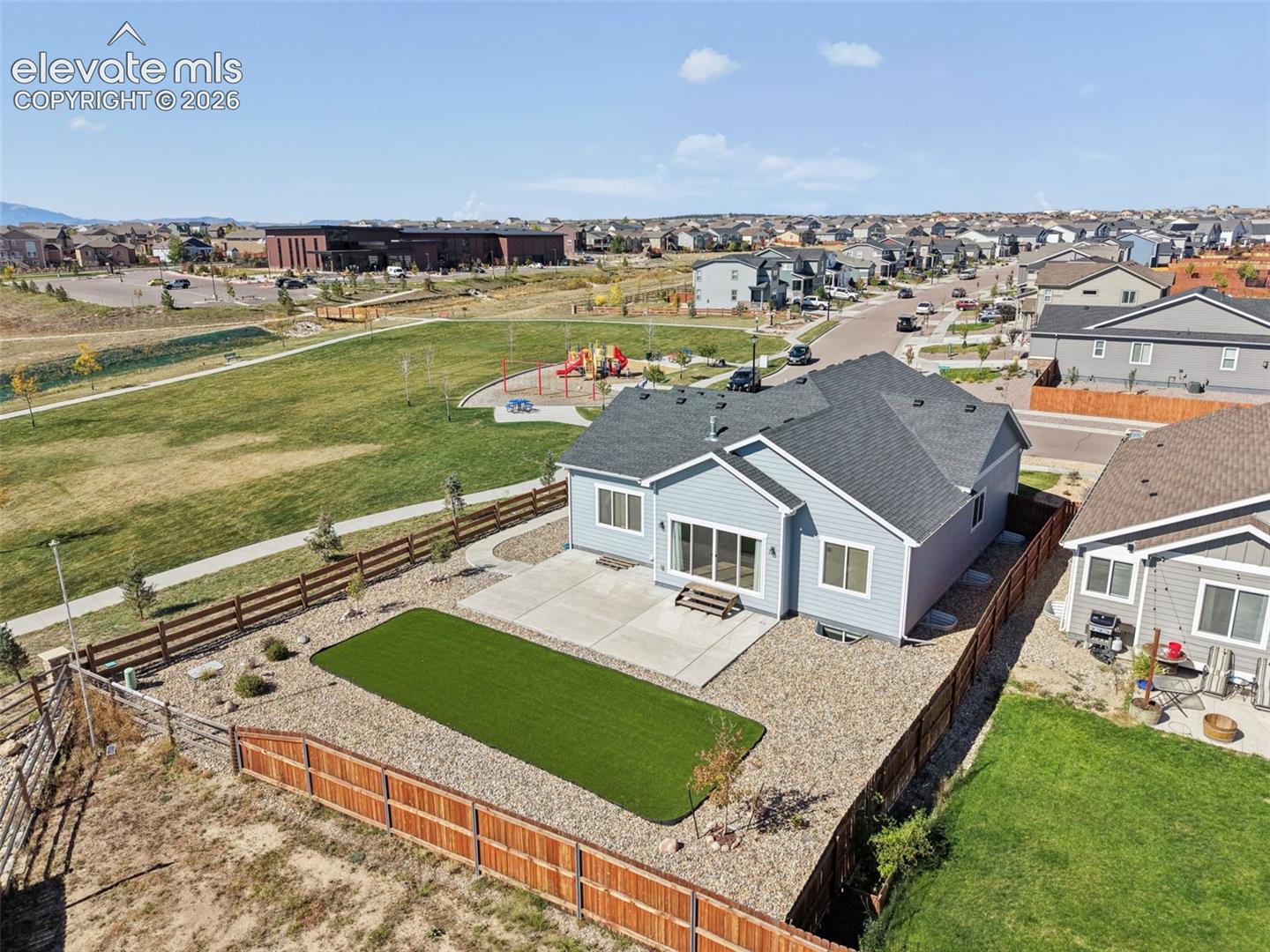 Exterior featuring a light blue siding finish, a concrete patio, a fenced backyard with artificial turf, and a gravel landscape