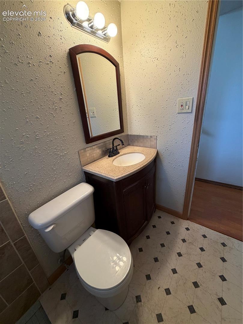 Single-basin vanity with dark wood-finish cabinetry, solid-surface countertop, arched wall-mounted mirror, and tile flooring with decorative inlay