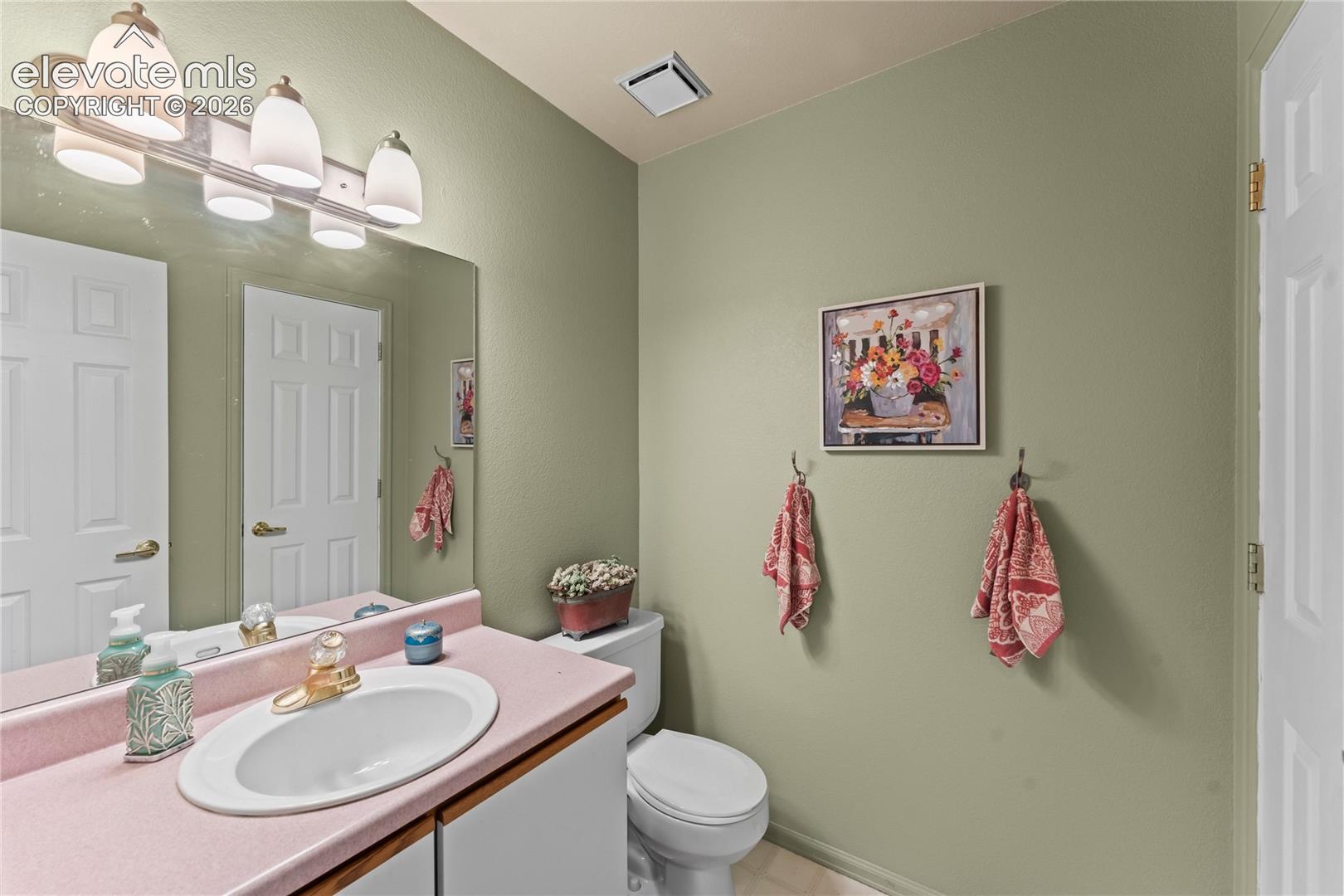 Extended vanity countertop with an integrated basin sink, mirrored wall, and overhead light fixture