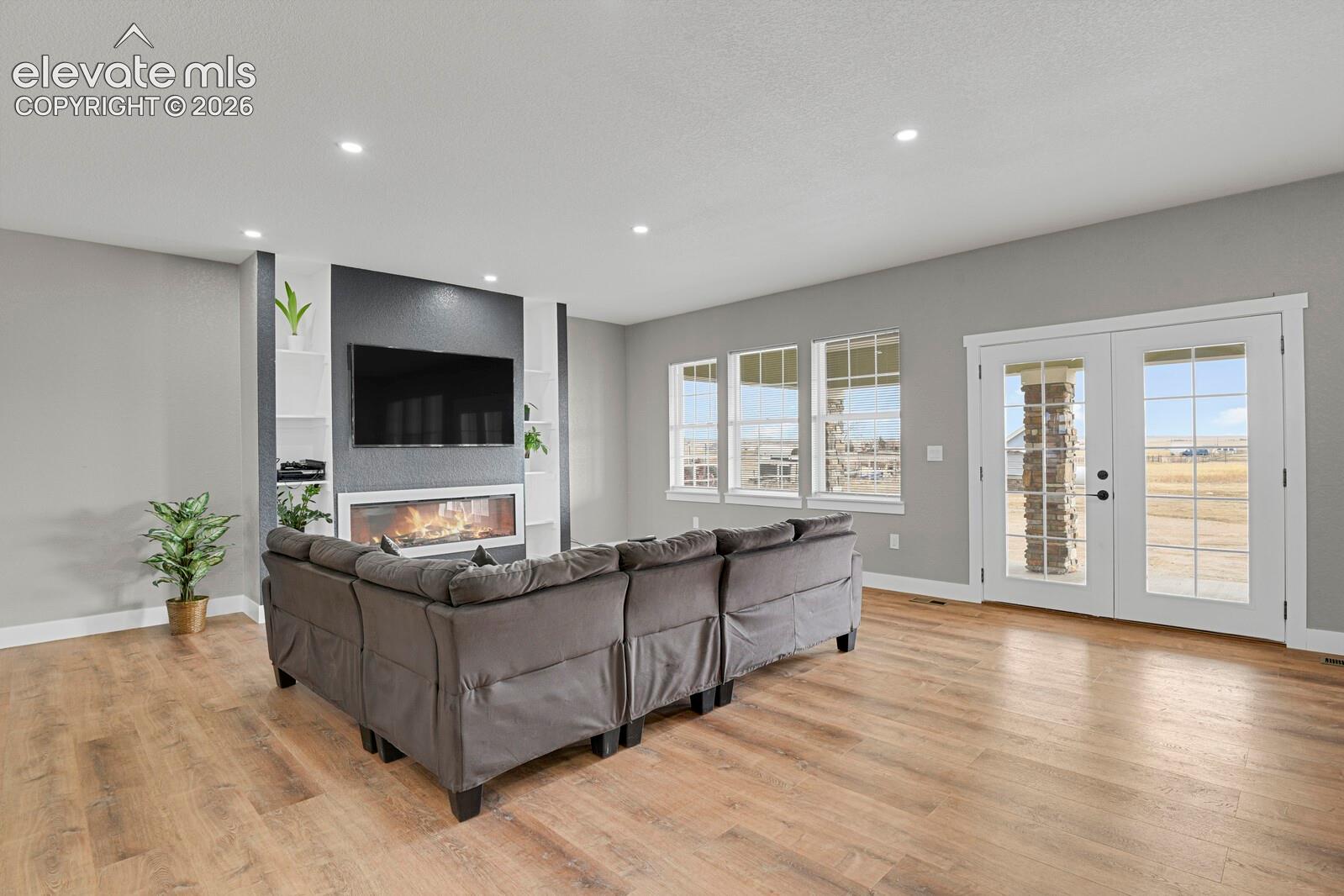 Living area featuring wood-finish flooring, a built-in electric fireplace with surrounding shelving, recessed lighting, and glass-paneled double doors
