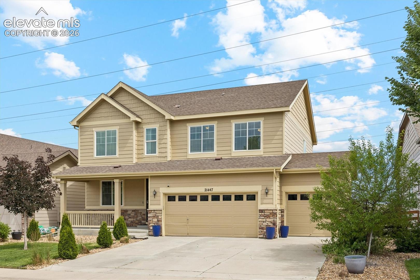 Two-story residence featuring a covered front porch with white railing, stone accents, and an attached two-car garage