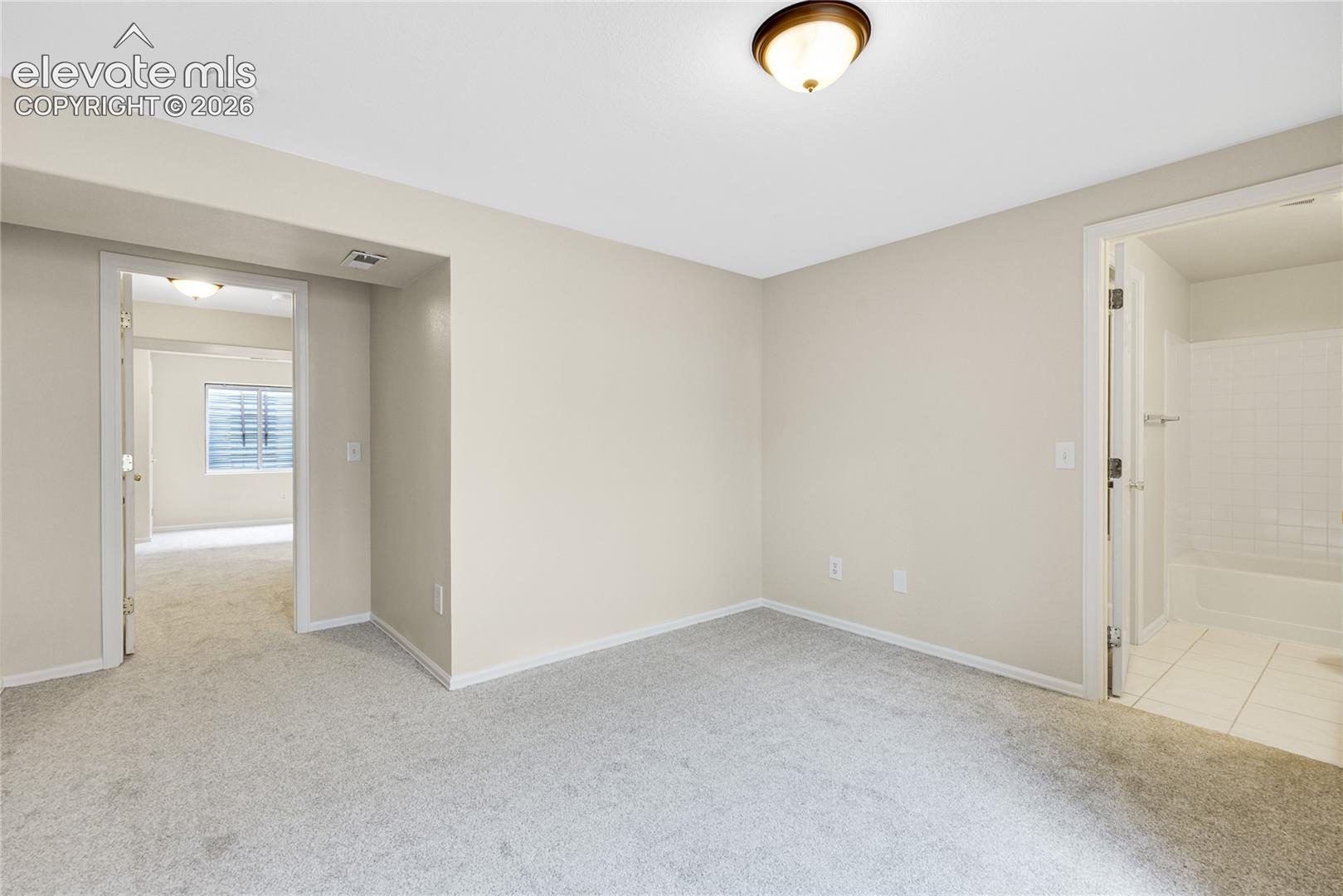 Neutral-toned interior room featuring wall-to-wall carpeting, a flush-mount ceiling light fixture, and ceramic tile flooring within the connected bathroom area