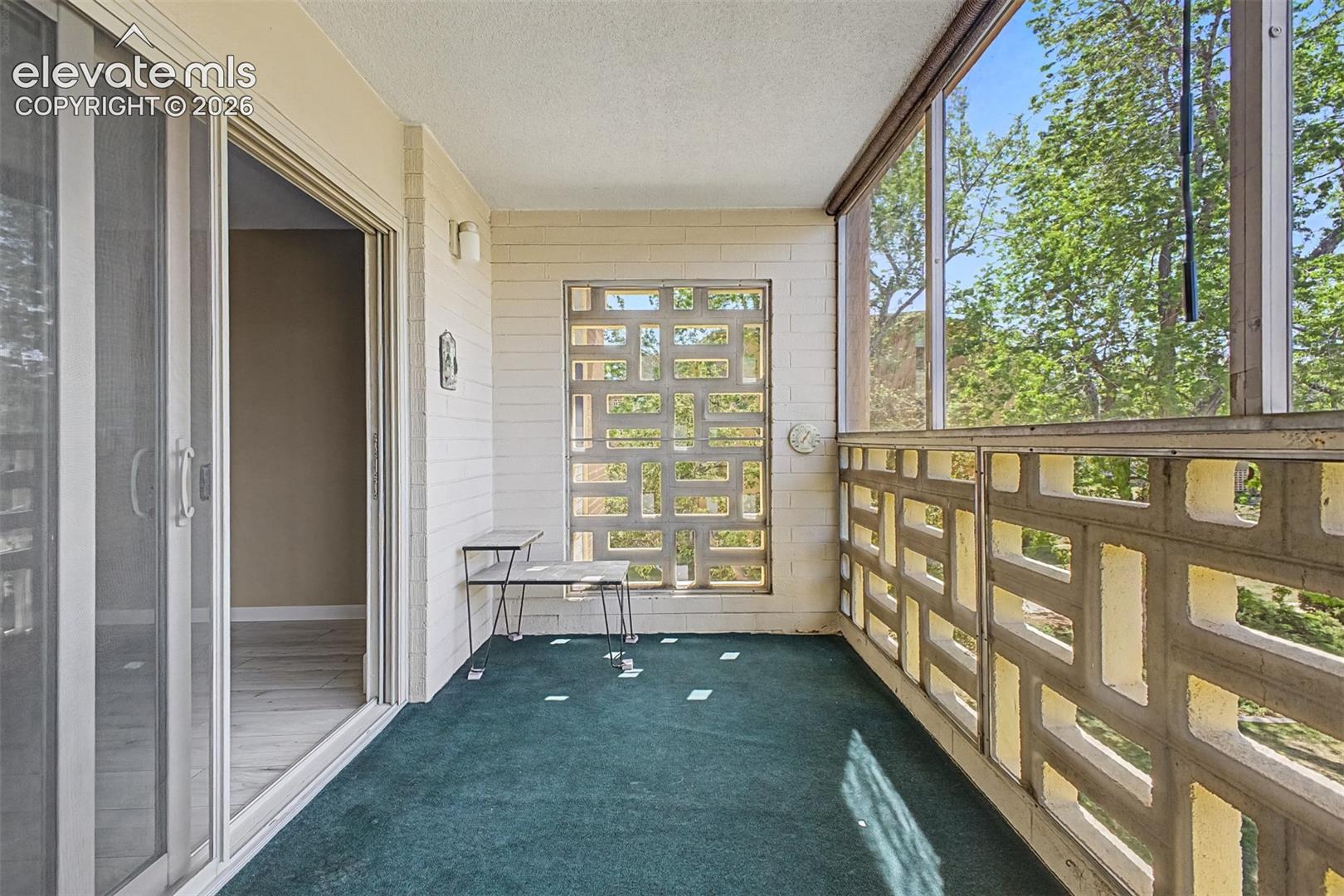 Enclosed balcony featuring patterned concrete block walls, screening, and teal carpeting