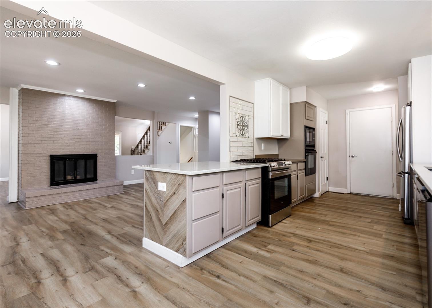 Expansive wood-finish flooring throughout, complemented by a brick fireplace with a black firebox