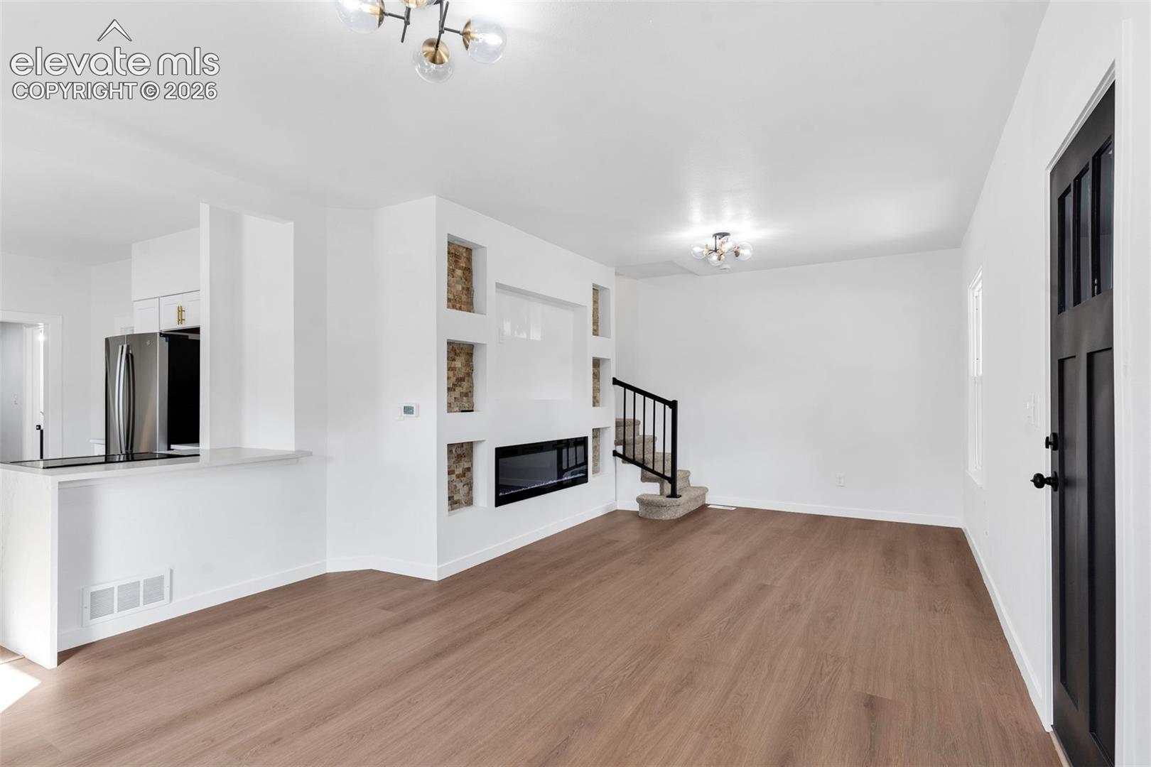 Open-concept interior featuring wood-finish flooring, a built-in media wall with a linear electric fireplace and decorative stone-tile insets, and a black paneled entry door