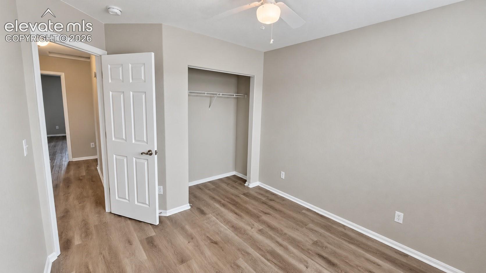 Neutral interior featuring wood-finish flooring, a ceiling fan with integrated lighting, and a closet with built-in shelving