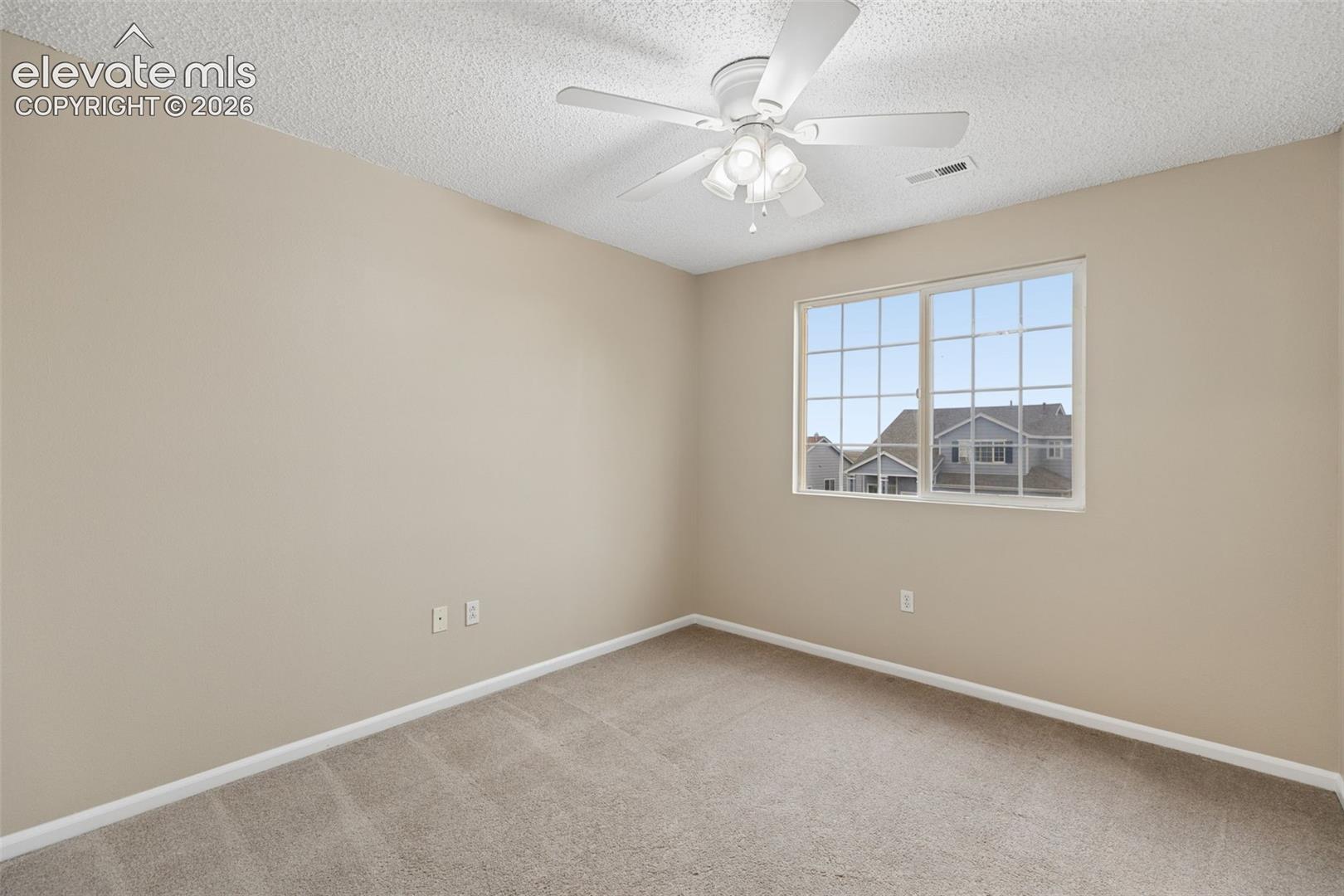 Neutral-toned interior space featuring wall-to-wall carpeting, a textured ceiling, a four-blade ceiling fan with integrated lighting, and a single-pane sliding window