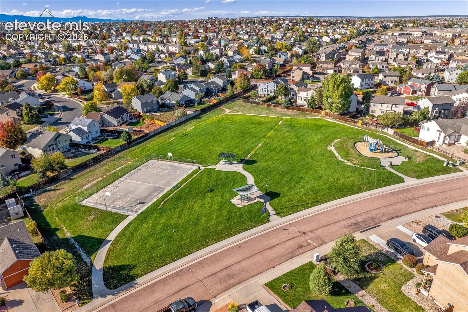 An elevated view highlights the neighborhood park's open lawn, paved recreation area + winding pathways, surrounded by established residential streets.