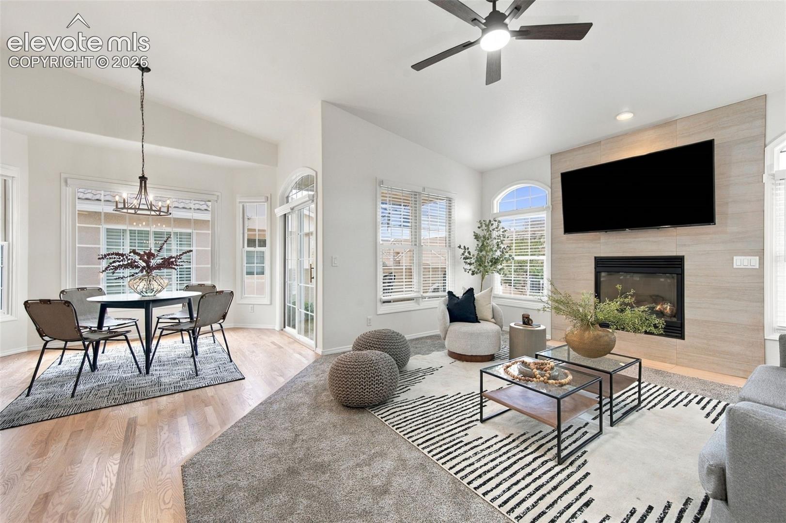 Open-concept interior featuring vaulted ceilings, a fireplace with floor-to-ceiling tile surround, wood-finish flooring, a contemporary chandelier, and arched windows