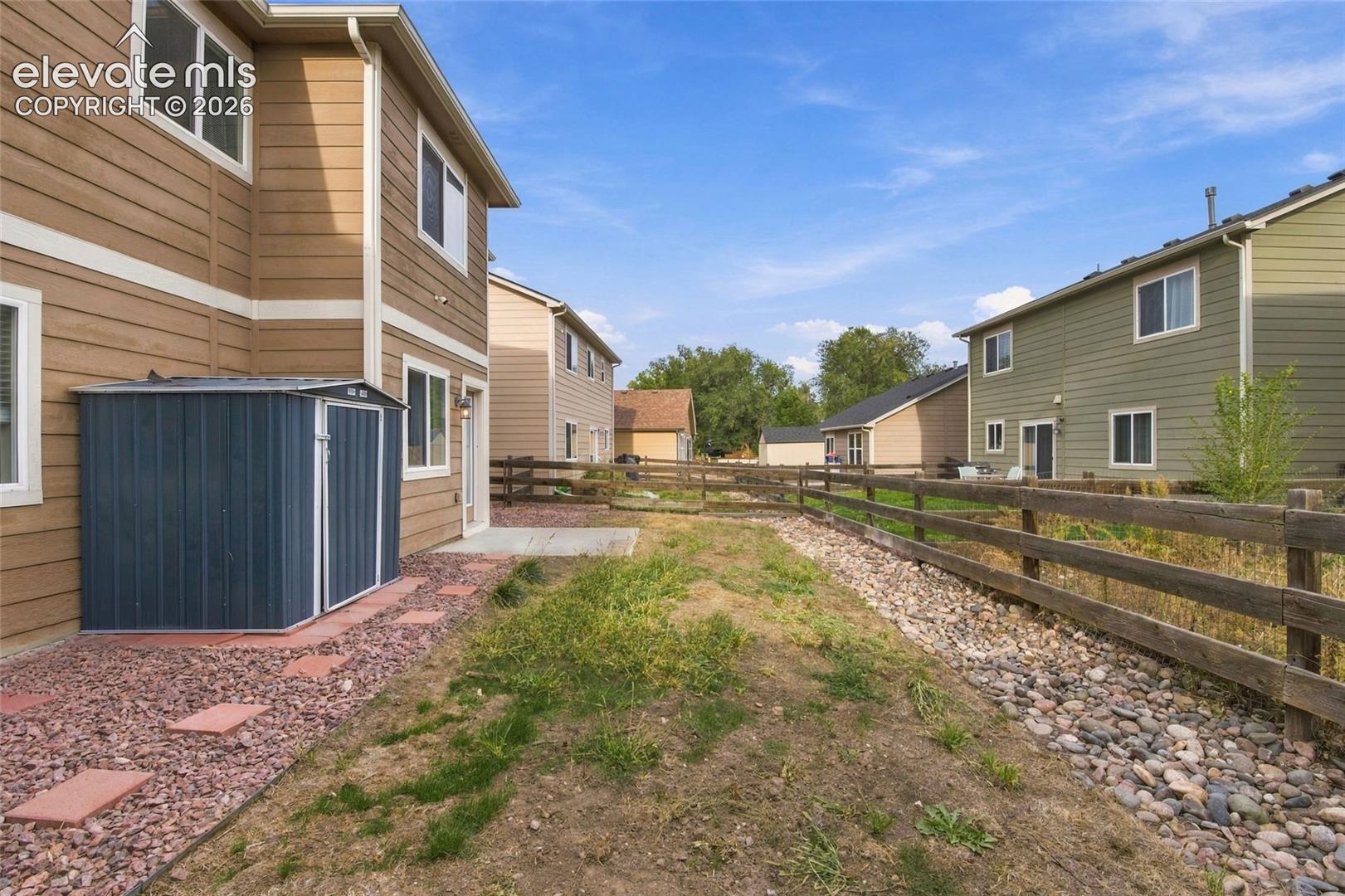 Rear yard featuring horizontal siding, a detached metal storage shed, concrete patio, stone ground cover, and wooden perimeter fencing