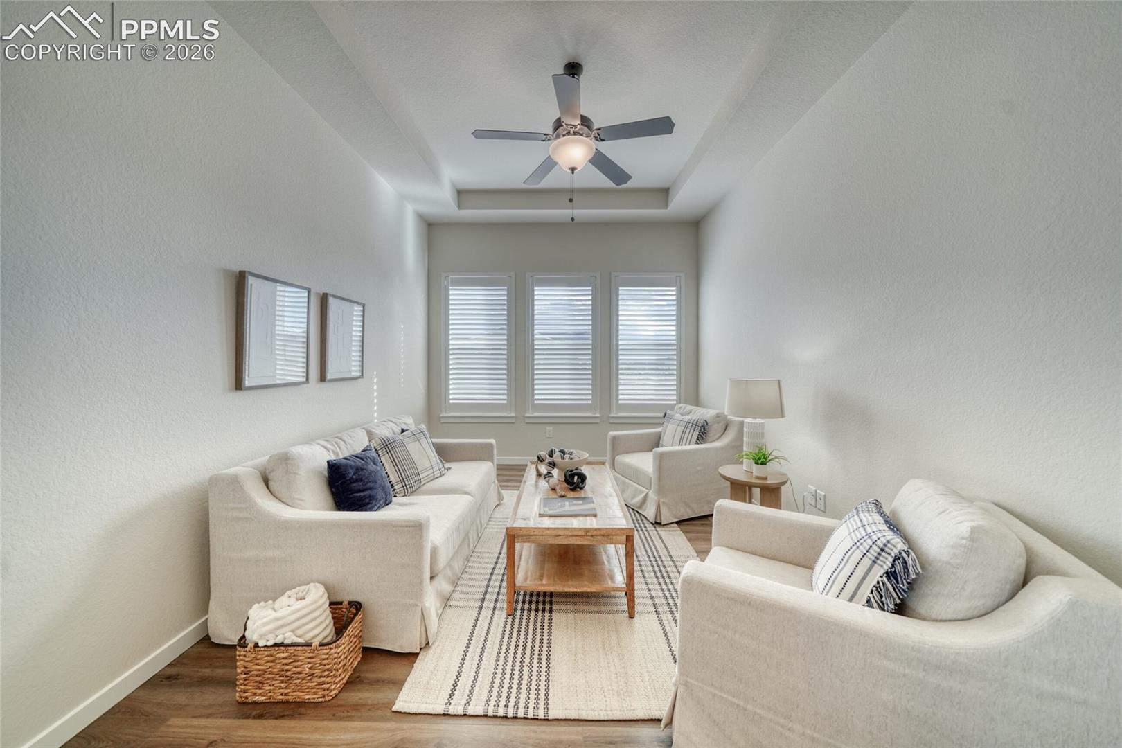 Living room with ceiling fan, wood finished floors, a textured wall, and a tray ceiling