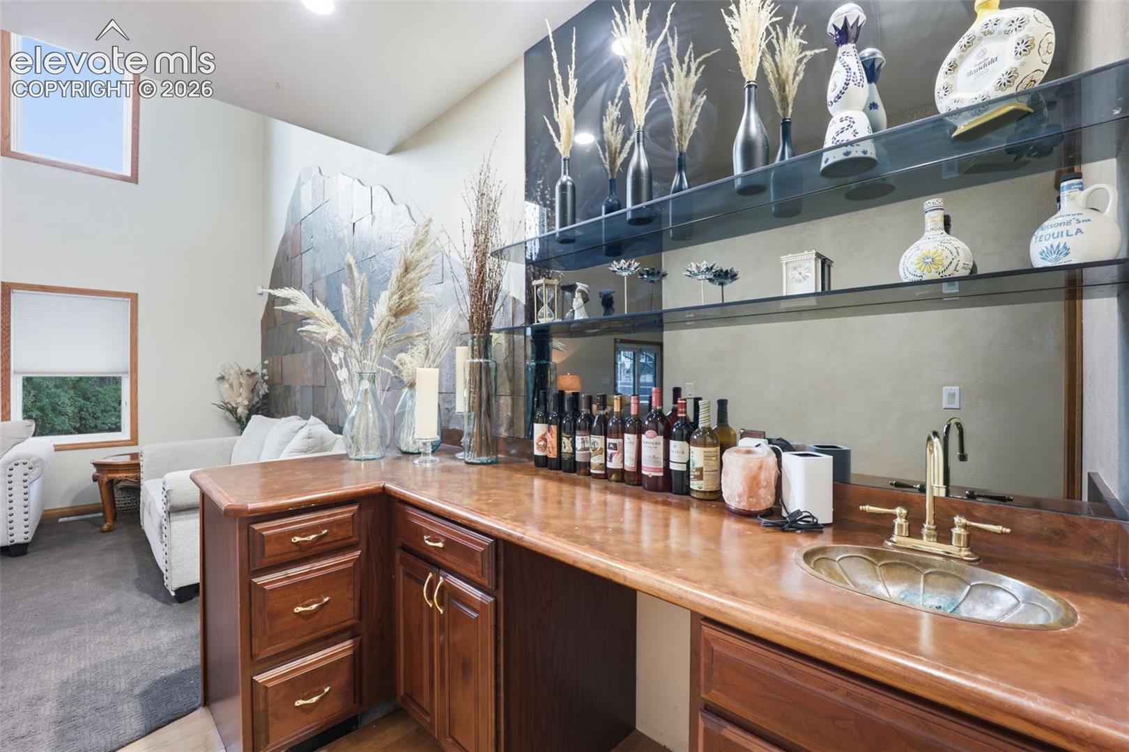 Built-in wet bar with wood cabinetry, a decorative basin sink, and brass fixtures