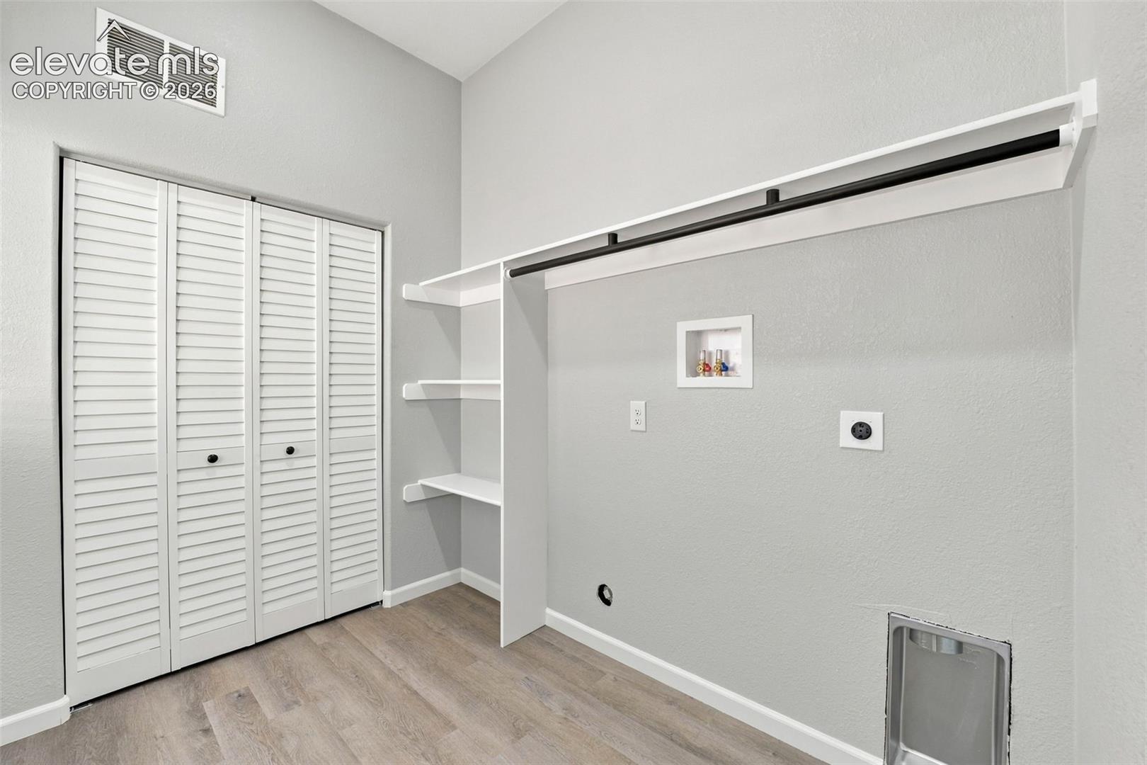 Laundry area featuring wood-finish flooring, built-in shelving, a clothes hanging rod, and louvered bifold closet doors