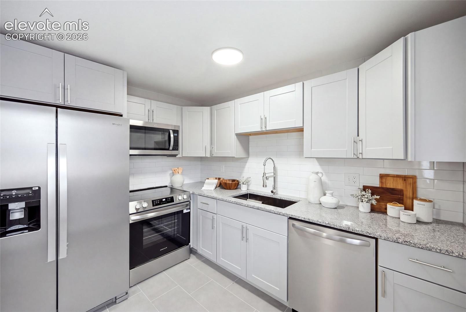 Stainless steel appliances, white shaker-style cabinetry, granite-patterned countertops, white subway tile backsplash, and light-toned floor tile