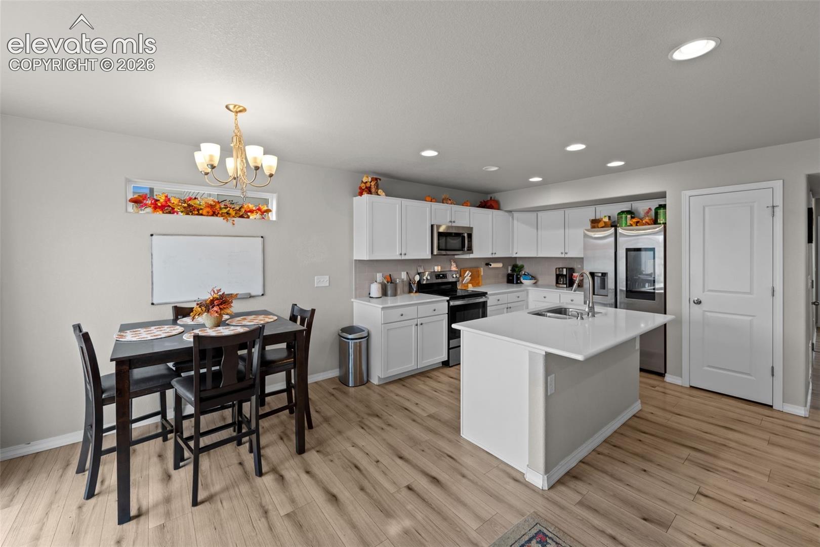 Bright kitchen with white cabinetry, stainless steel appliances, a center island with sink, recessed lighting, and wood-finish flooring