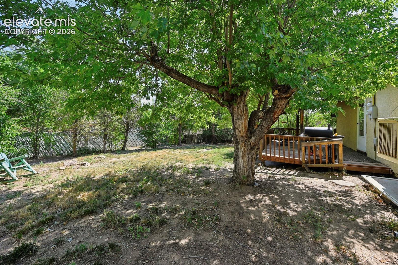 Spacious backyard featuring a large mature tree, wood deck, and partial fencing