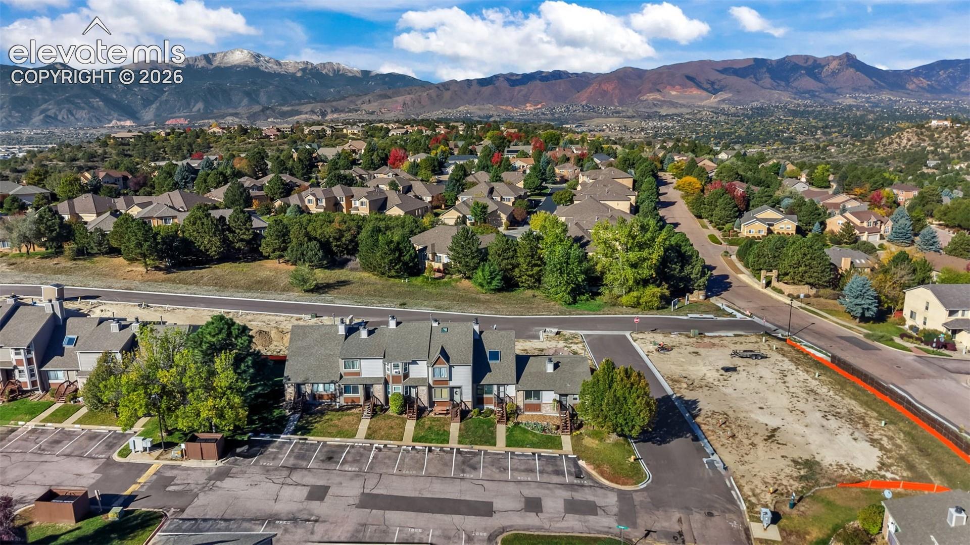 Multi-unit residential complex featuring asphalt parking, gabled rooflines, neutral siding, and a prominent mountain range backdrop
