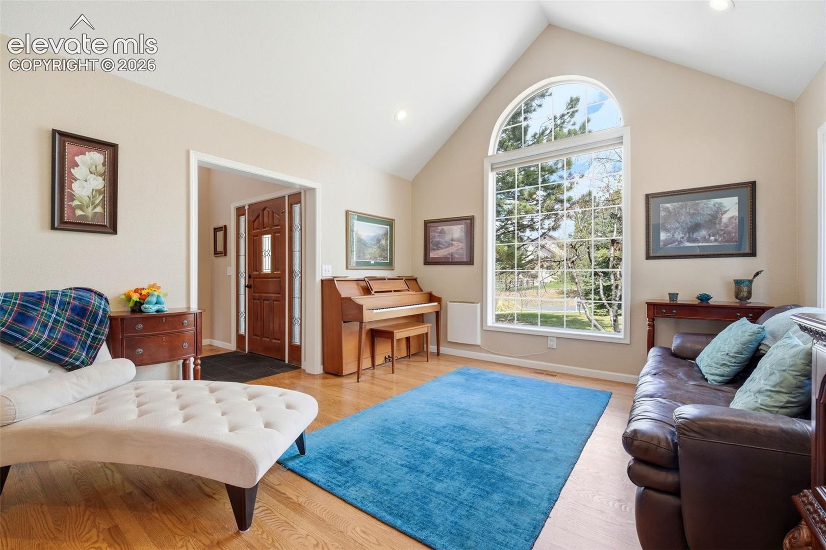 Vaulted ceiling living area featuring a large arched window with grid detailing, wood-finish flooring, a paneled front door with sidelights, and recessed lighting